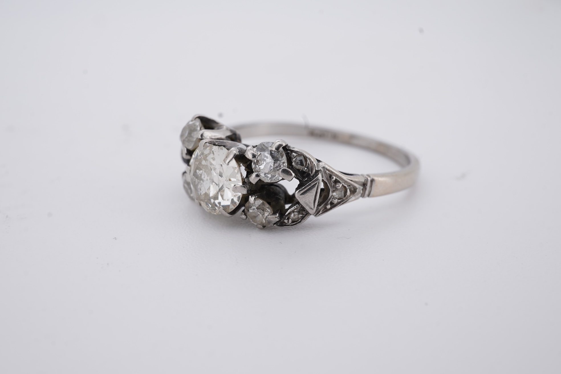 A white metal (stamped platin) and single stone diamond ring, flanked by four smaller diamonds and rose cut diamond chip set shoulders, size P, gross weight 3.8 grams.